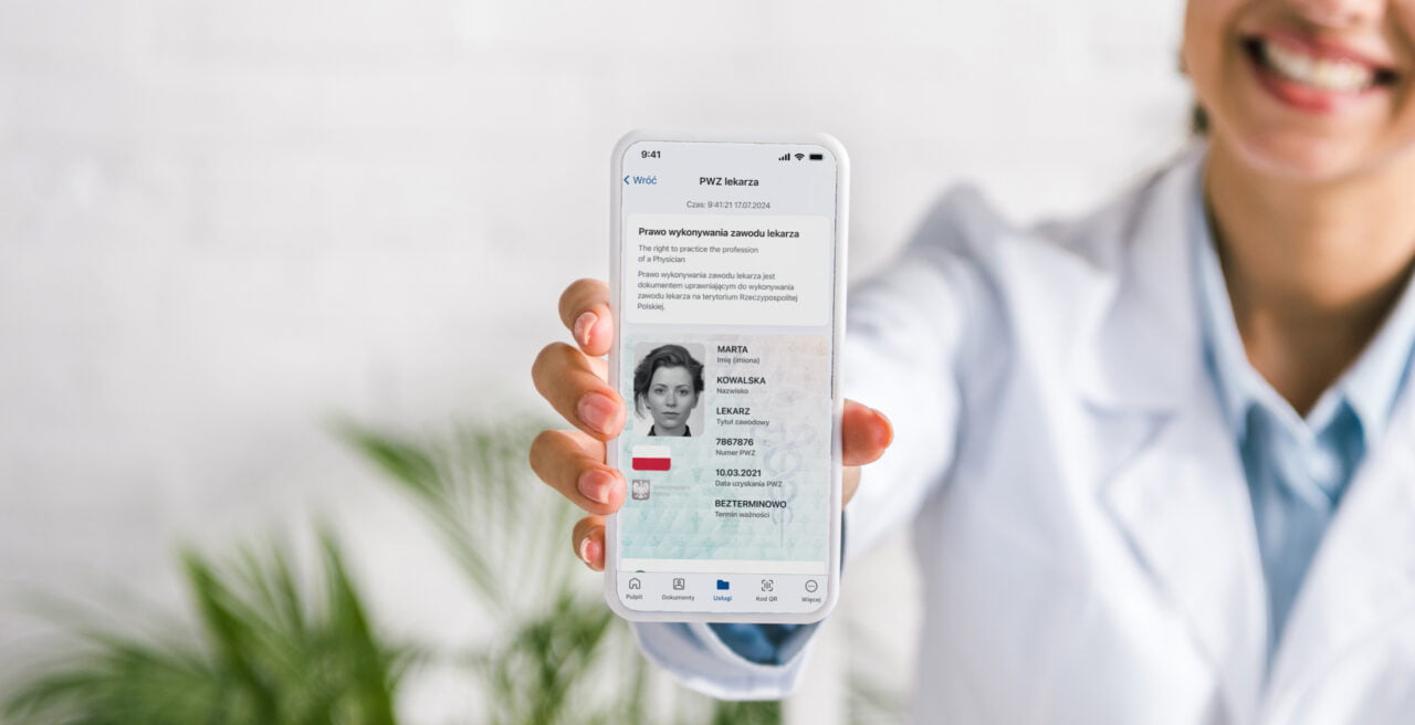 Lekarka trzymająca smartfon z wyświetloną cyfrową wersją prawa wykonywania zawodu lekarza.