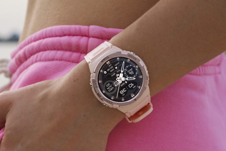 Zbliżenie na różowy smartwatch na ręce osoby ubranej w różowe spodenki.