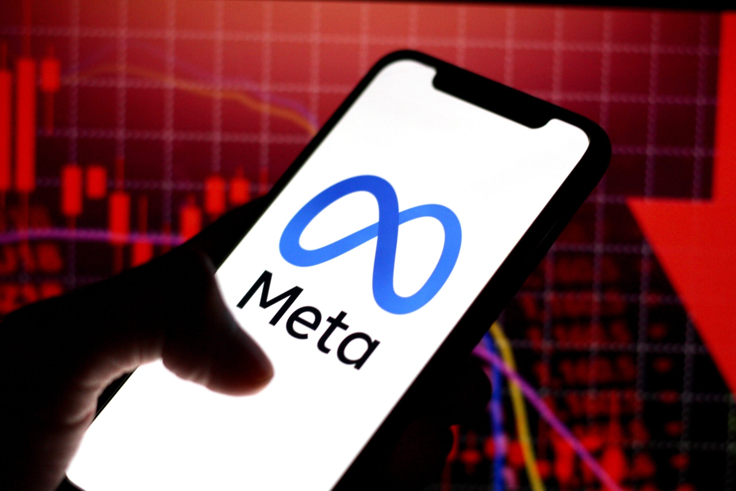 Logo Meta na ekranie smartfona, w tle wykresy giełdowe.