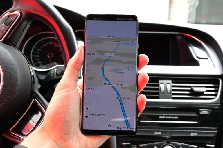 Osoba trzymająca smartfon z włączoną nawigacją GPS, wewnątrz samochodu.