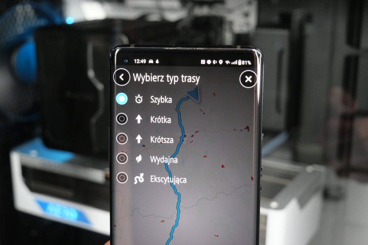 Smartfon z aplikacją GPS pokazującą wybór typu trasy, z opcjami: Szybka, Krótka, Krótsza, Wydajna, Ekscytująca.