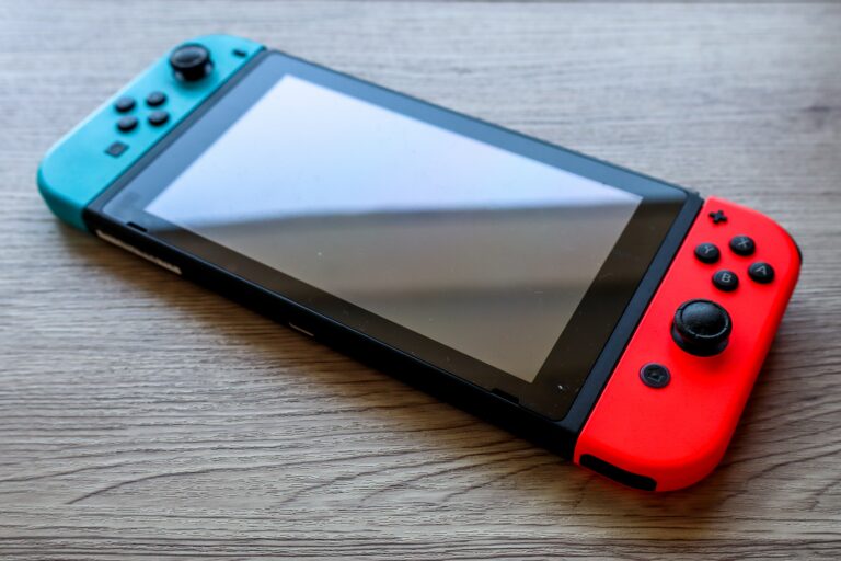 Konsola do gier Nintendo Switch leżąca na drewnianym stole z niebieskim i czerwonym Joy-Conem.