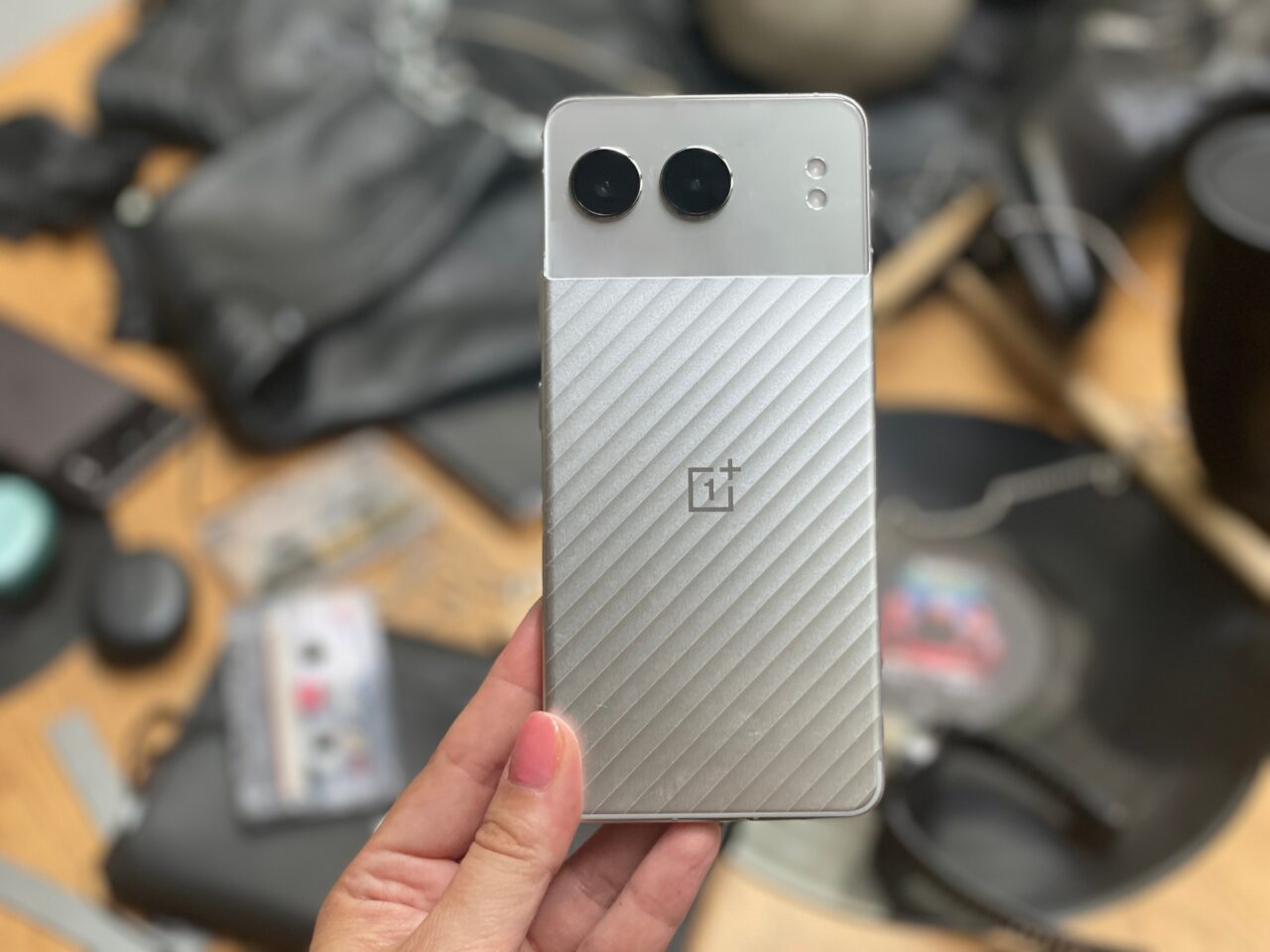 Srebrny smartfon OnePlus trzymany w dłoni, w tle rozmyte przedmioty.