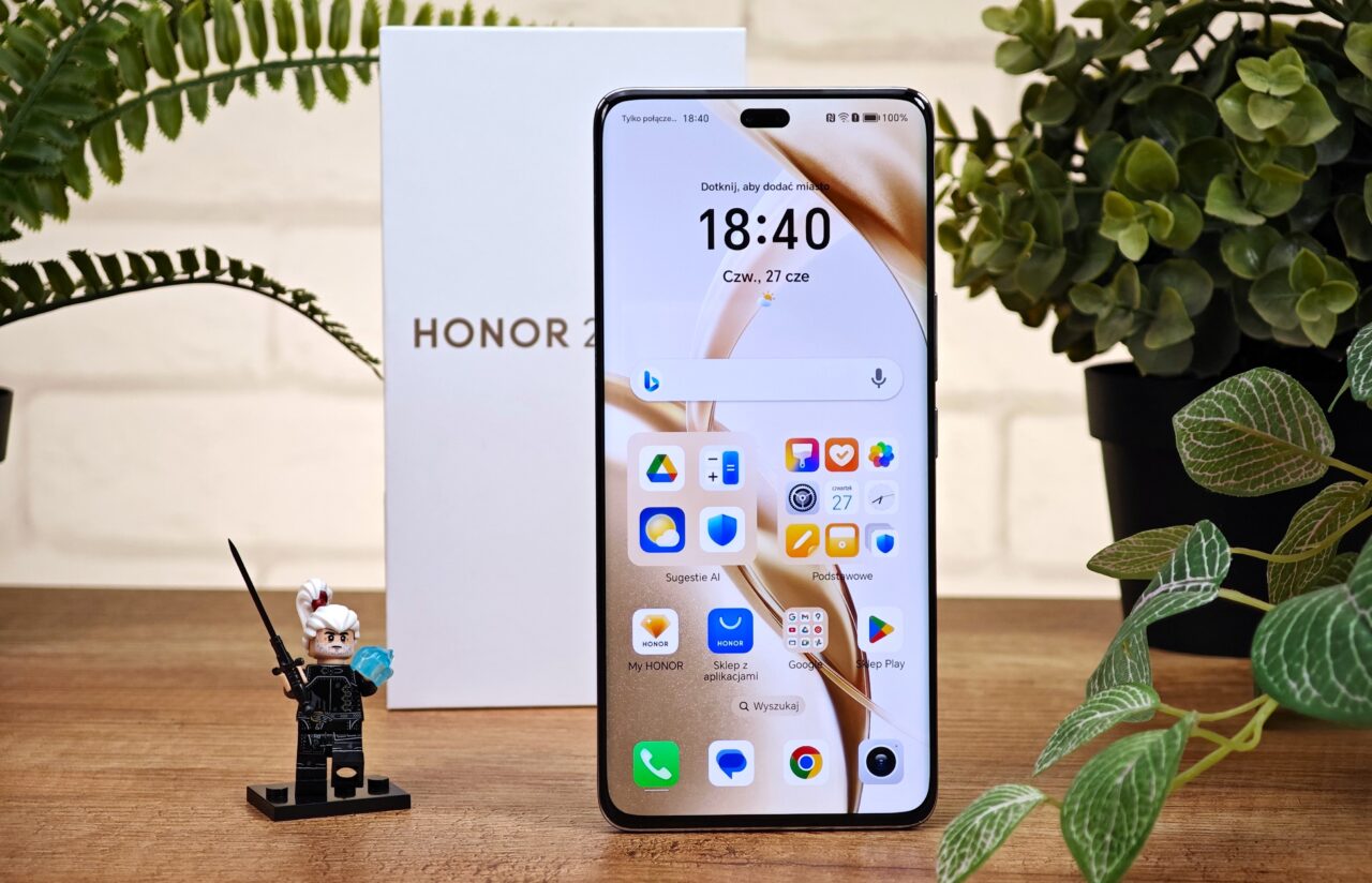 Smartfon Honor 200 Pro wyświetlający ekran główny, w tle pudełko z napisem „HONOR 200 pro” oraz rośliny, na pierwszym planie figurka LEGO wiedźmin.