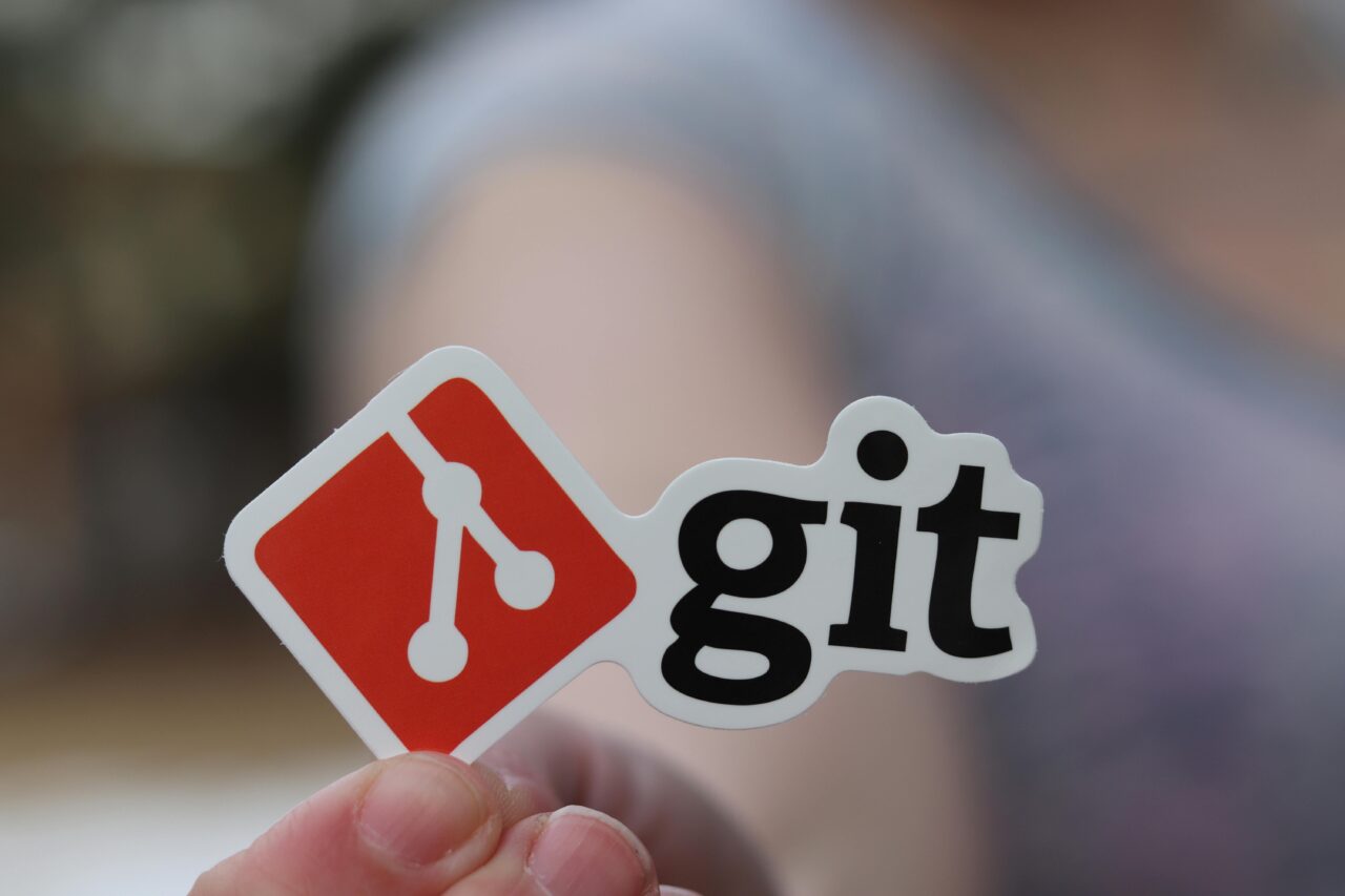 DevOps. Naklejka z logo Git trzymana przez osobę w tle.