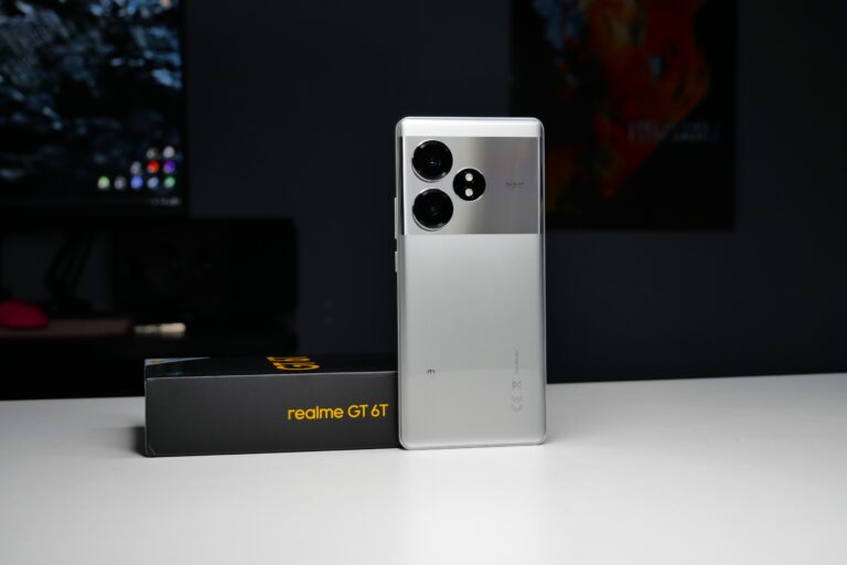 Smartfon Realme GT 6T w kolorze srebrnym stojący na białym stole, obok czarnego pudełka z żółtym napisem "realme GT 6T".