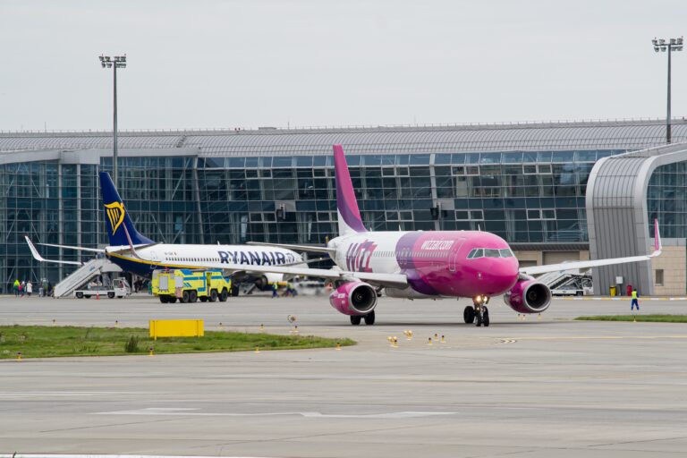 Samoloty linii Ryanair i WizzAir na płycie lotniska przed nowoczesnym terminalem.