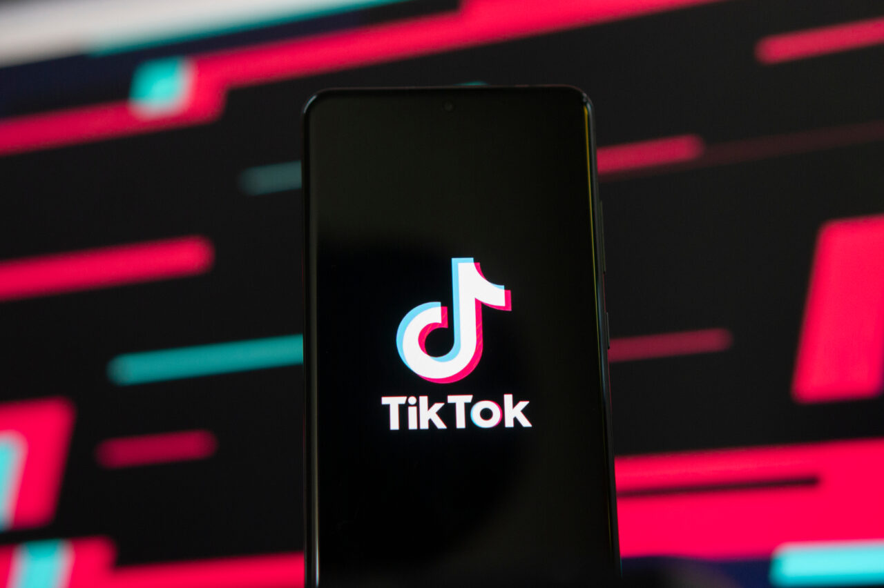 Logo TikTok na ekranie smartfona na tle kolorowych wzorów.