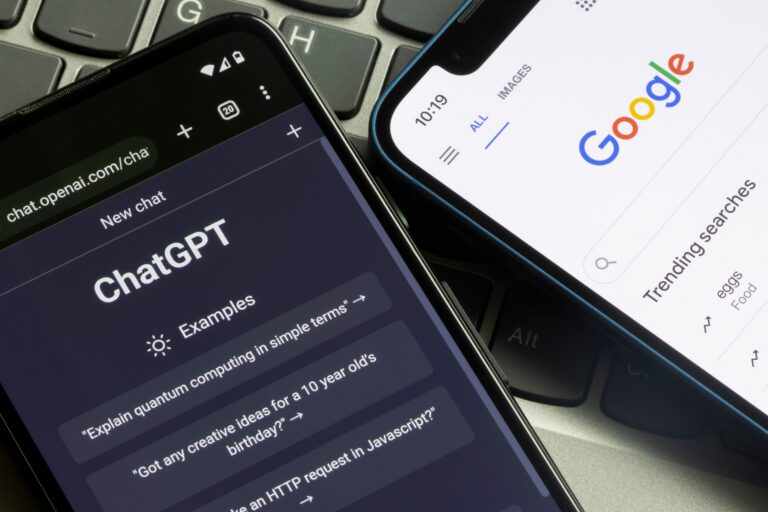 Dwa smartfony, jeden z otwartą aplikacją ChatGPT, drugi z przeglądarką z wyszukiwarką Google, leżą na klawiaturze laptopa.