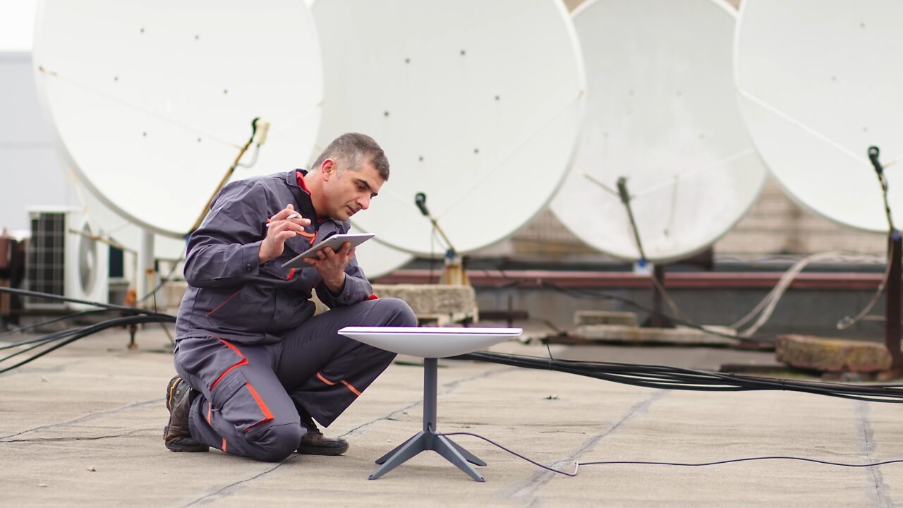 Starlink. Technik montujący antenę satelitarną na dachu używający tabletu.