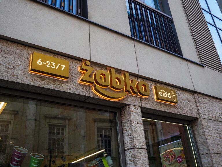 Szyld sklepu Żabka z informacją o godzinach otwarcia oraz logo Żabka Café.