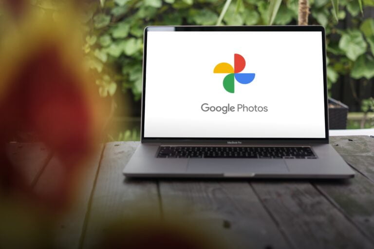 Ekran laptopa z logo Google Photos na białym tle, w tle zielone rośliny.
