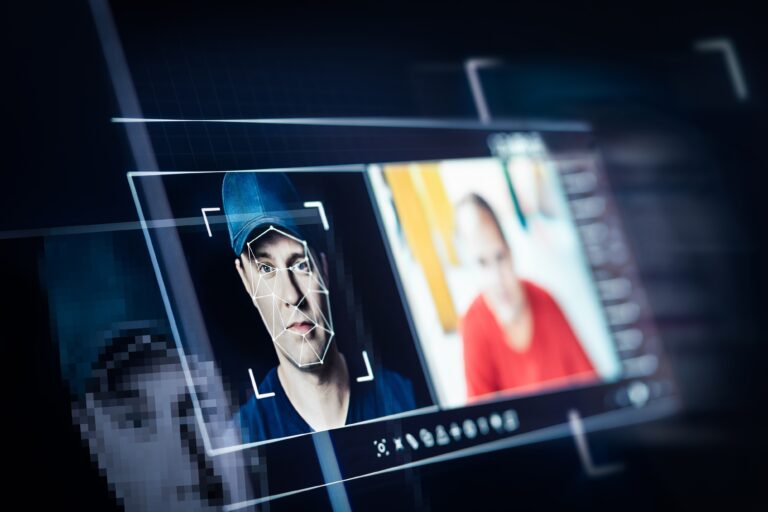 Ekran komputera pokazujący rozpoznawanie twarzy dwóch mężczyzn, jeden z widoczną siatką w konturach twarzy.