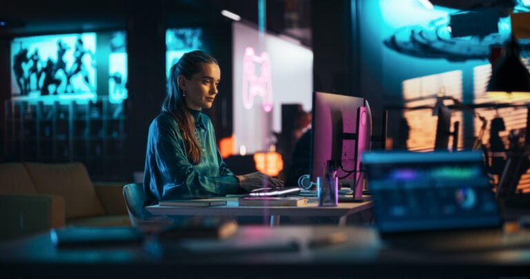 Kobieta przy biurku pracująca na komputerze w dobrze oświetlonym, nowoczesnym biurze.