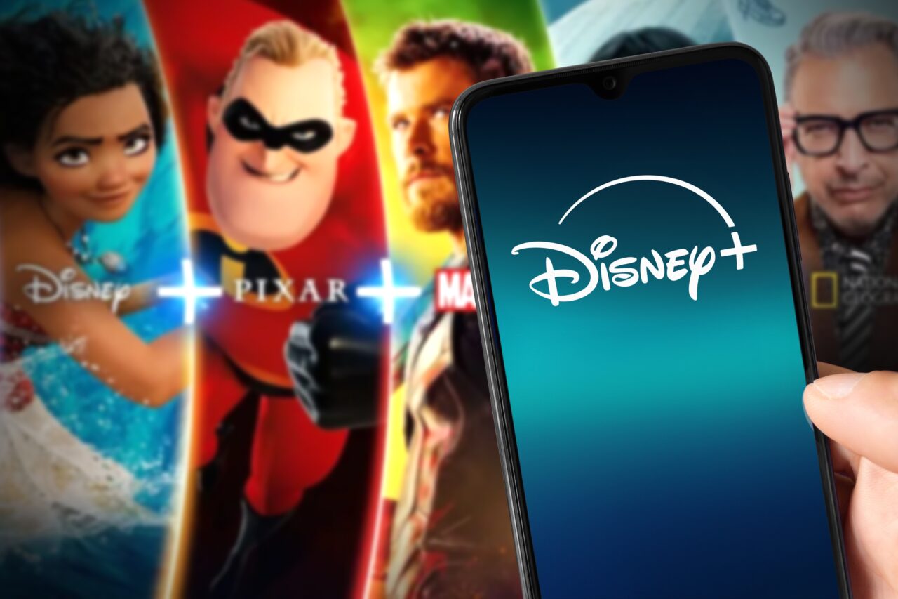 Ekran telefonu z logo Disney+, w tle postacie z filmów Disney, Pixar, Marvel i National Geographic.