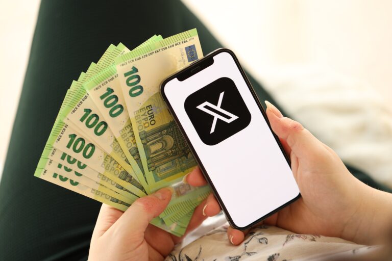 Osoba trzymająca wachlarz banknotów 100 euro i telefon komórkowy z logo aplikacji X.