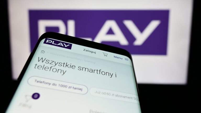 Przybliżenie smartfona wyświetlającego stronę internetową Play z ofertą smartfonów, w tle widoczny rozmazany napis "PLAY".