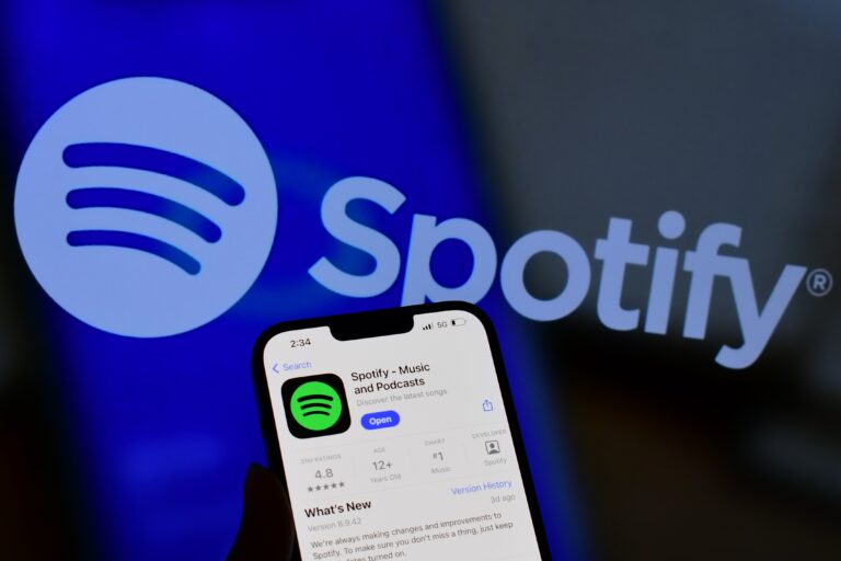 Logo Spotify oraz ekran telefonu z aplikacją Spotify w tle.