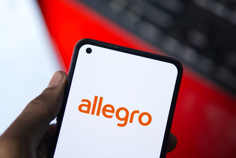 Logo Allegro na ekranie smartfona trzymanego w dłoni.