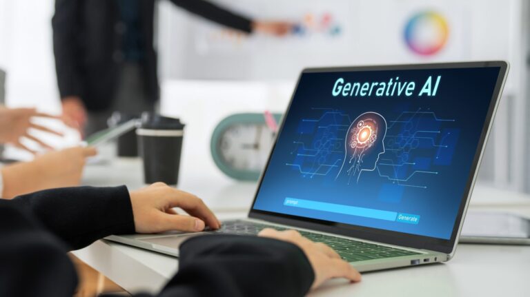 Osoba korzystająca z laptopa z wyświetloną grafiką dotyczącą AI-generatywnej sztucznej inteligencji. W tle inne osoby pracujące przy biurku.