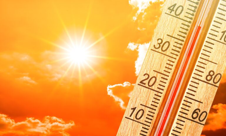 Termometr wskazujący wysoką temperaturę na tle jasnego słońca i pomarańczowego nieba.