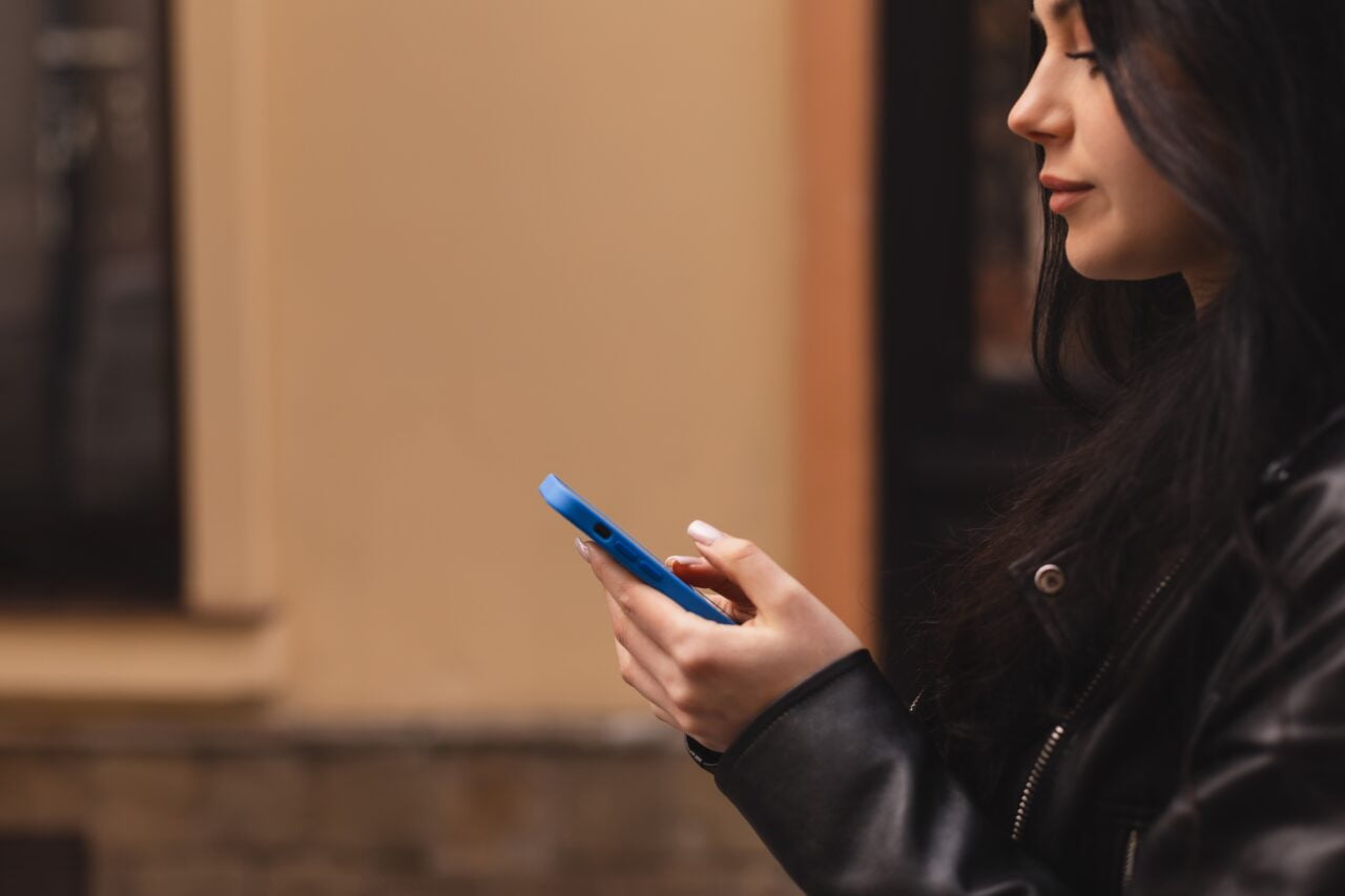 Kobieta w czarnej kurtce trzymająca telefon komórkowy, który można zaliczyć do grupy urządzeń, jaką są smartfony