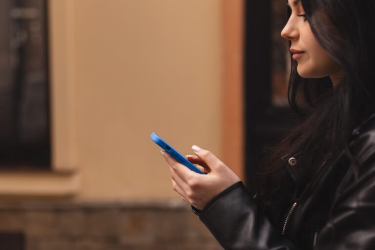 Kobieta w czarnej kurtce trzymająca telefon komórkowy.