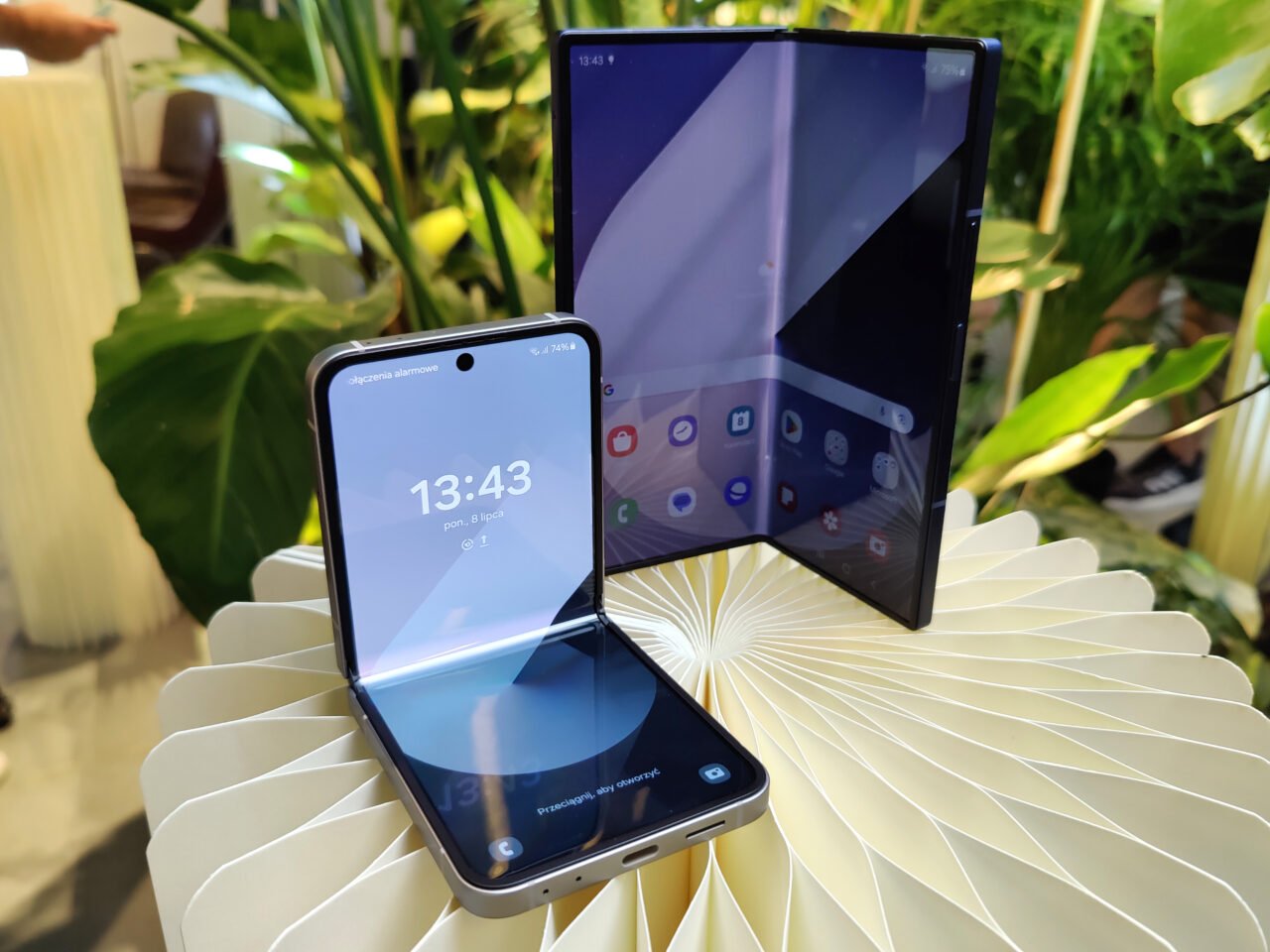 Premierowe promocja z okazji premiery Samsung Galaxy Z Fold6 i Flip6. Dwa składane smartfony na tle roślinności, jeden otwarty pionowo, drugi poziomo.