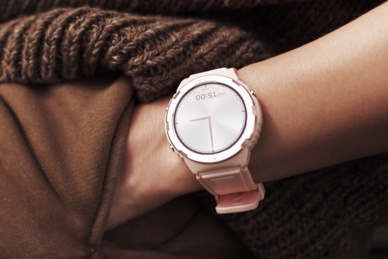 Różowy zegarek na ręce, w tle brązowy sweter.