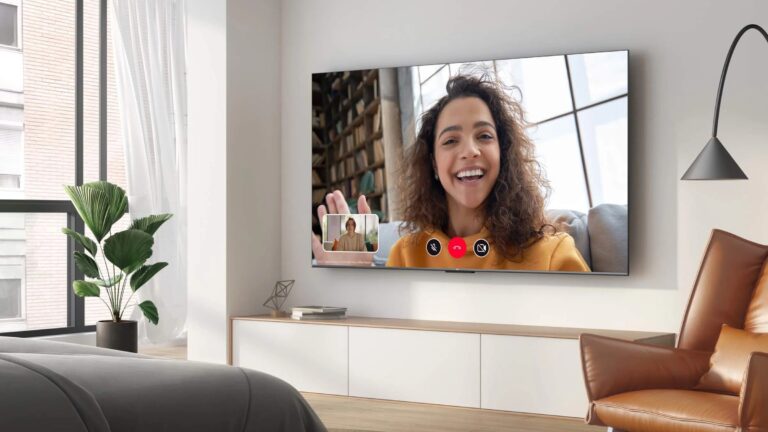 Pokój dzienny z dużym telewizorem na ścianie, na którym widać rozmowę wideo pomiędzy dwiema osobami.