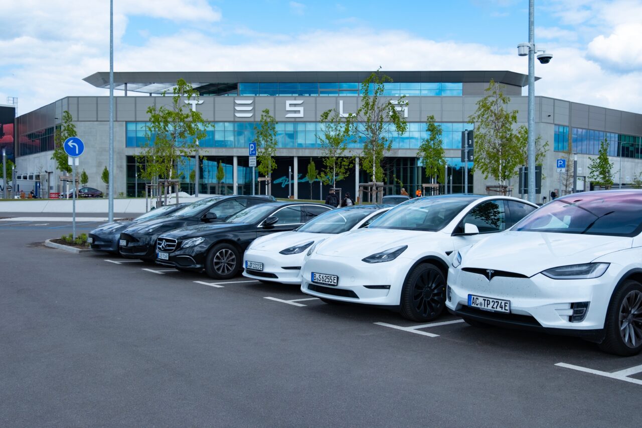 Samochody elektryczne marki Tesla. Parking przed budynkiem Tesla z zaparkowanymi samochodami Mercedes i Tesla.