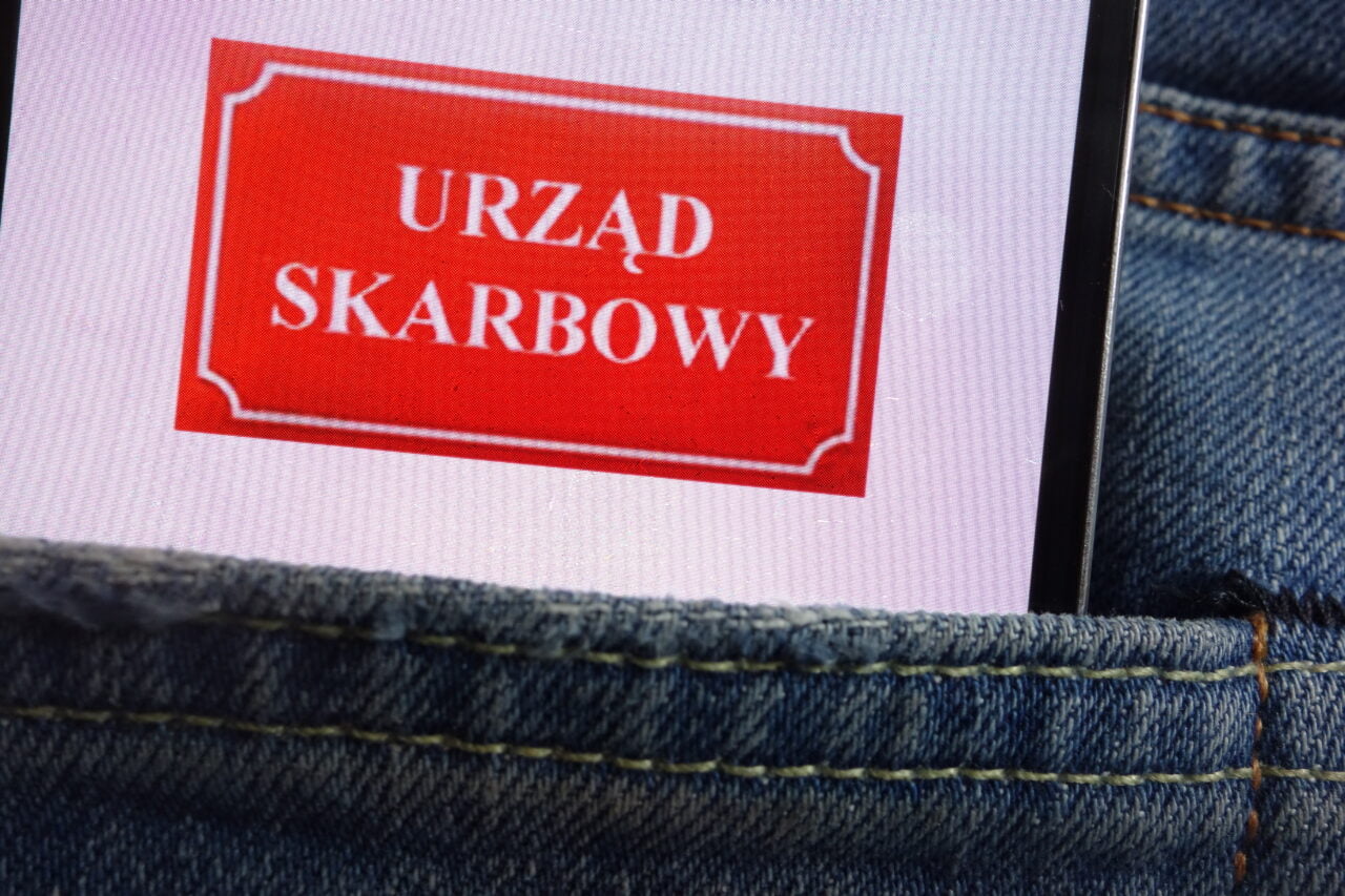 Ekran telefonu z napisem "URZĄD SKARBOWY" wystający z kieszeni dżinsów.