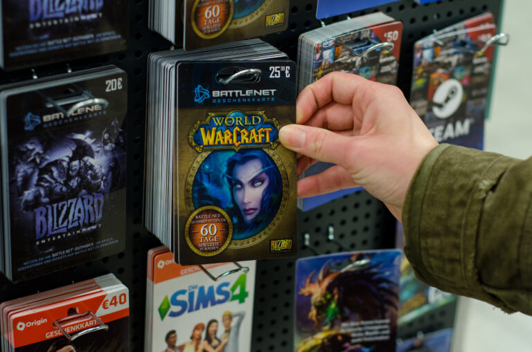 Osoba trzymająca kartę prezentową World of Warcraft na stojaku z kartami prezentowymi w sklepie Blizzard AI.