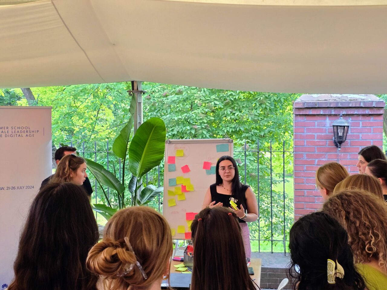 Huawei Summer School for Female Leadership. Grupa młodych ludzi podczas warsztatów na świeżym powietrzu, kobiety omawiające treści na tablicy z kolorowymi karteczkami.