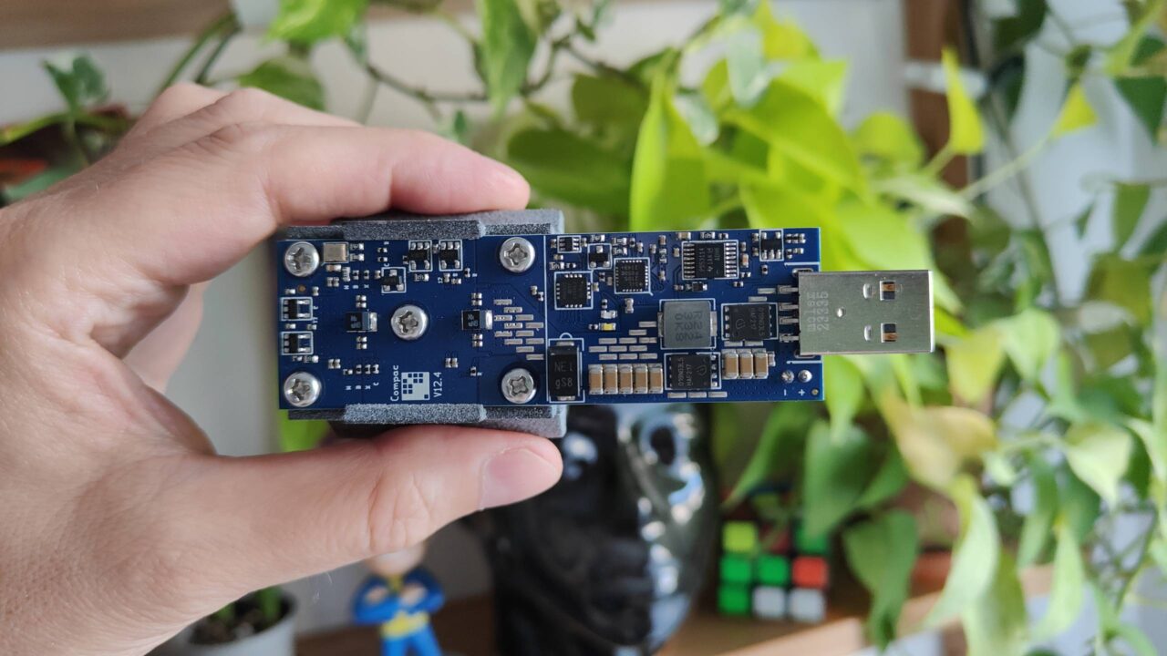 koparka USB dla kryptowalut. Osoba trzymająca niebieską płytkę elektroniczną z portem USB na tle roślin.