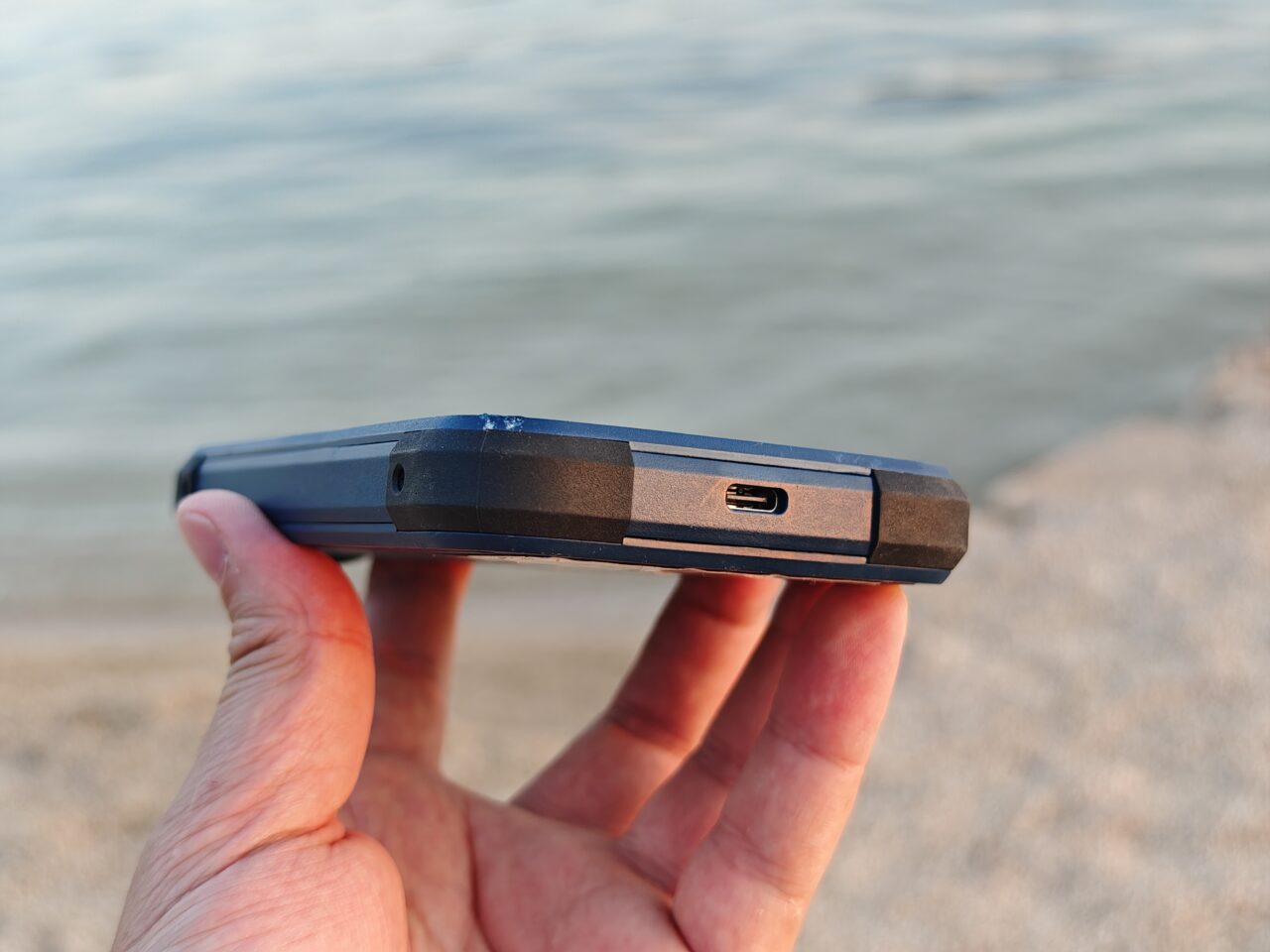 Dłoń trzymająca Acer Connect Enduro 3 z portem USB-C na tle plaży.