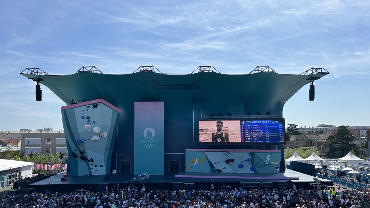 Scena z tłumem ludzi, wspinaczka sportowa, duża tablica wyników, logo Paryż 2024 Olympijskie.