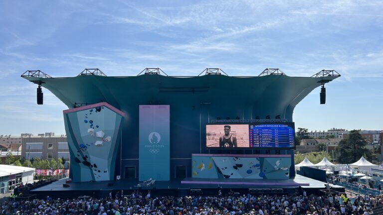 Scena z tłumem ludzi, wspinaczka sportowa, duża tablica wyników, logo Paryż 2024 Olympijskie.