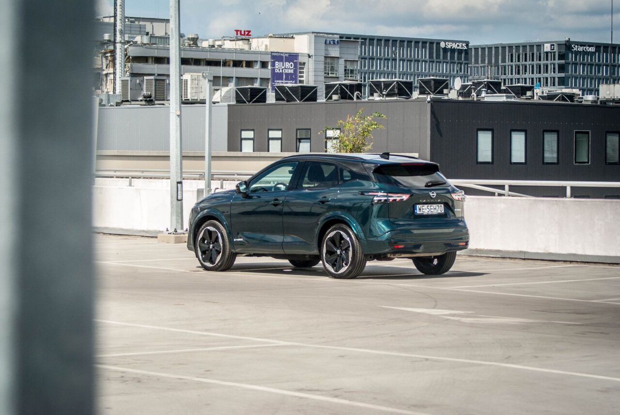 Ciemnozielony samochód SUV na parkingu na dachu z budynkami w tle.