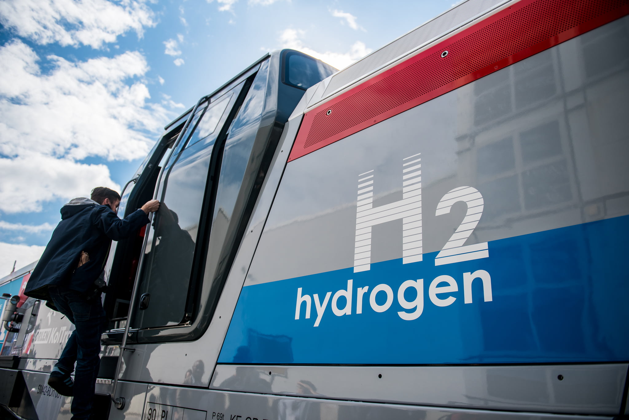 Człowiek wchodzi po schodach do pociągu na wodór, napisy "H2 hydrogen" na boku pojazdu.