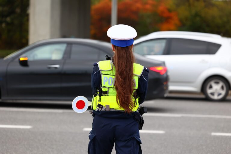 Policjantka w kamizelce odblaskowej i czapce policyjnej kierująca ruchem na drodze.