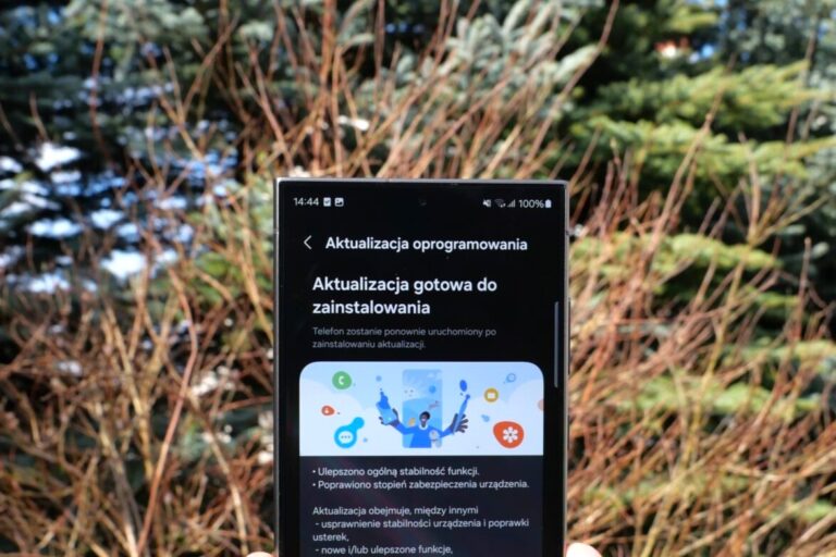 Telefon z ekranem informującym o gotowej aktualizacji oprogramowania, trzymany na tle roślin.