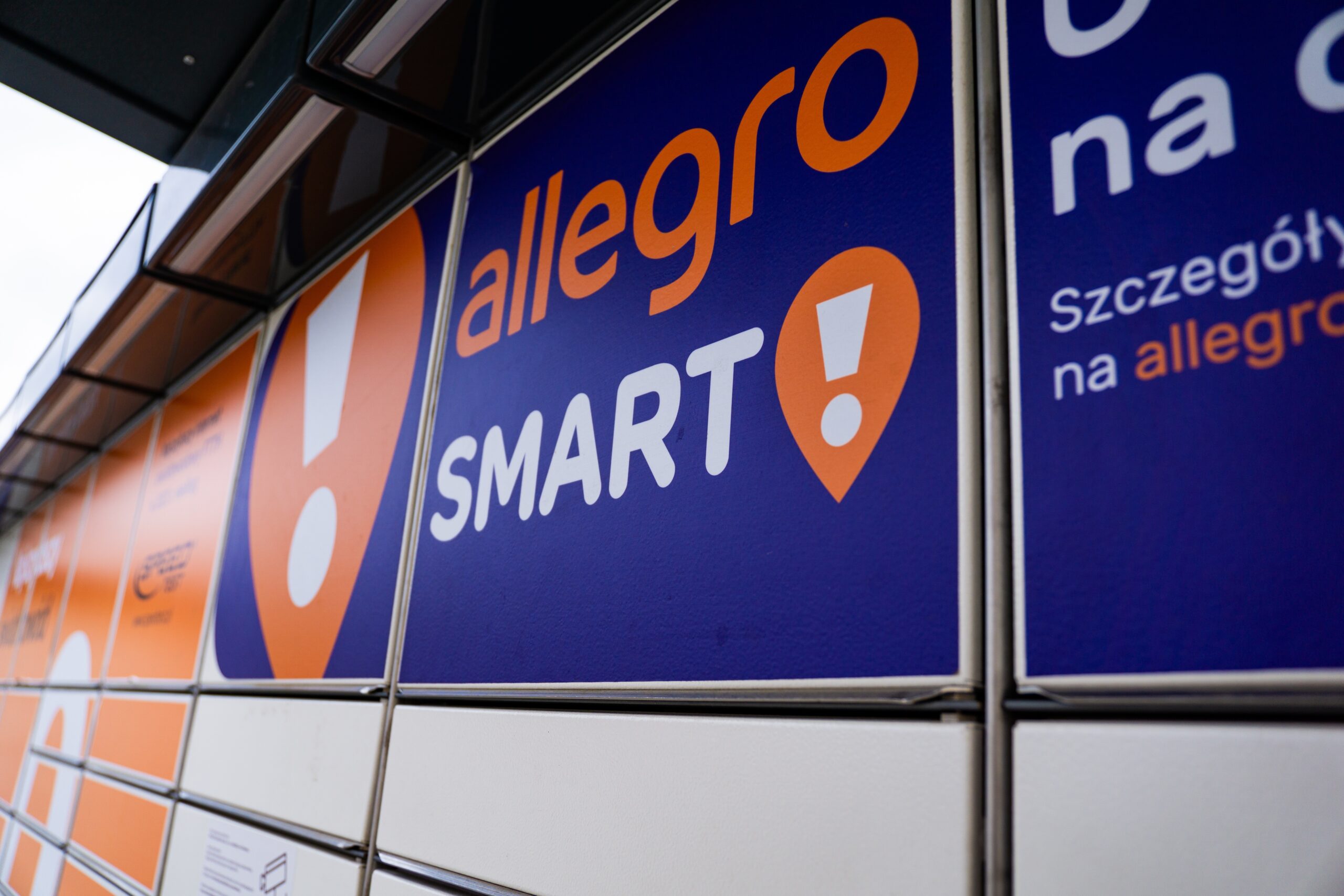 Automat paczkowy Allegro Smart! z bliska, z logo w kolorze pomarańczowym i białym na niebieskim tle.