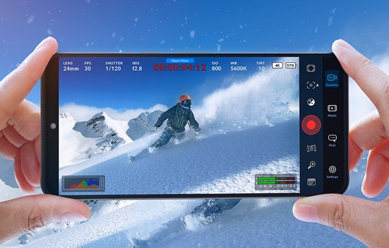 aplikacja Blackmagic camera - Osoba trzymająca smartfon nagrywający snowboardzistę na ośnieżonym stoku górskim. Na ekranie wyświetlają się ustawienia nagrywania.