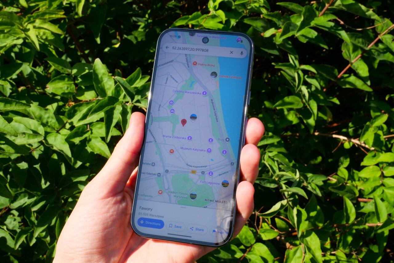 Osoba trzymająca smartfon z widokiem mapy lokalizacyjnej, w tle zielone liście.