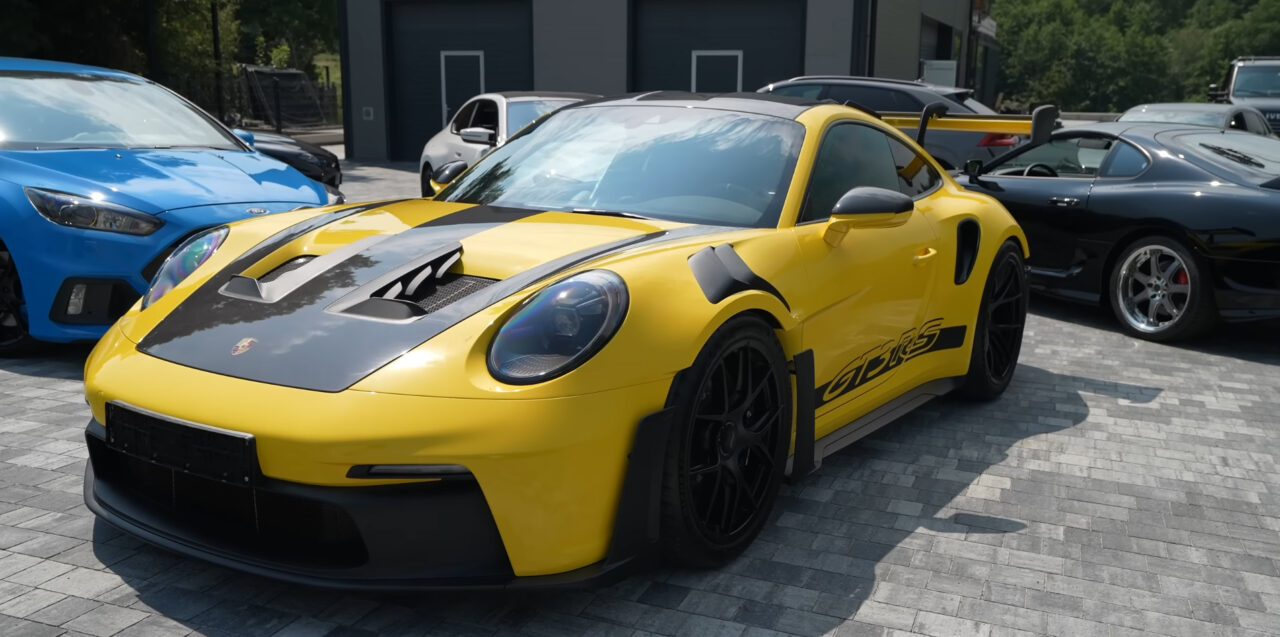 Jasnożółty samochód sportowy Porsche 911 GT3 RS zaparkowany na kostce brukowej obok innych samochodów.