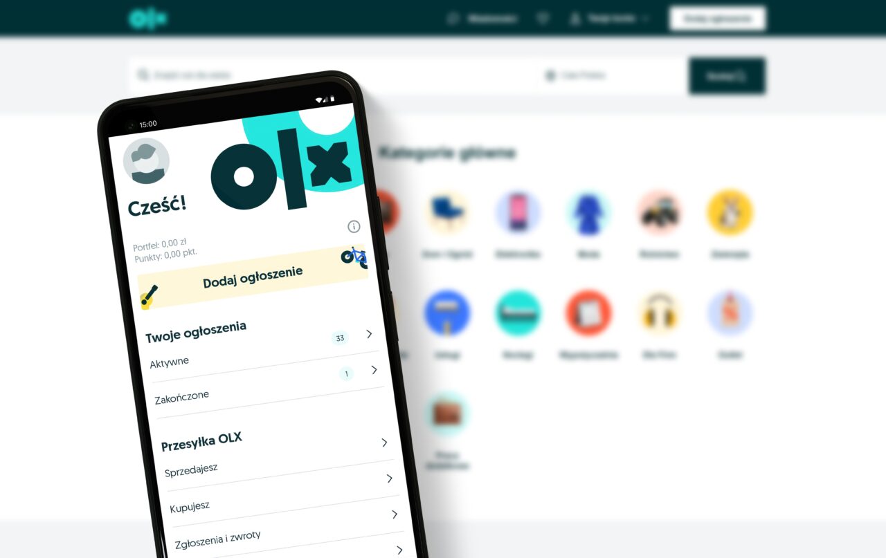 Aplikacja OLX na telefonie komórkowym z widocznym panelem użytkownika i opcją dodania ogłoszenia na tle pulpitu kategorii głównych.