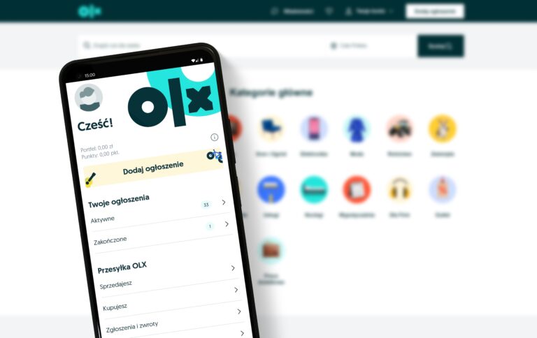 Aplikacja OLX na telefonie komórkowym z widocznym panelem użytkownika i opcją dodania ogłoszenia na tle pulpitu kategorii głównych.