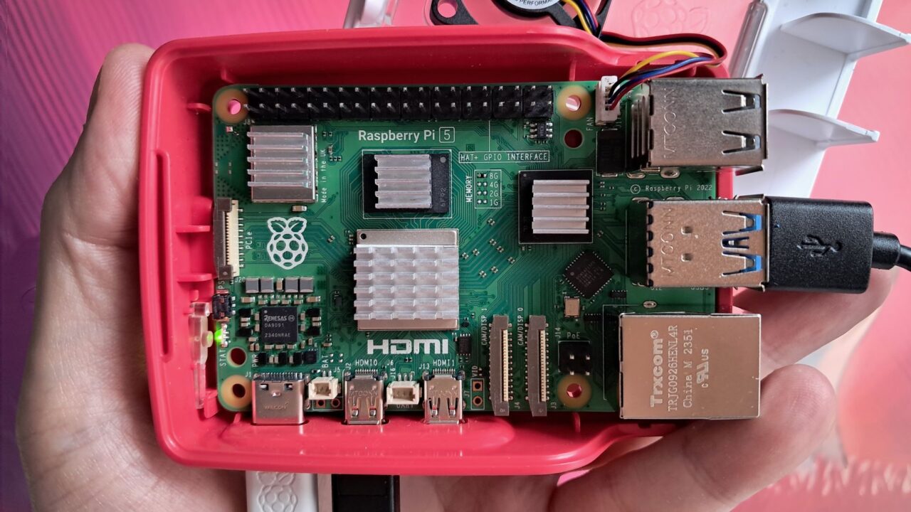 Raspberry Pi 5 w czerwonej obudowie, porty HDMI, USB, Ethernet, z podłączonym przewodem zasilającym.