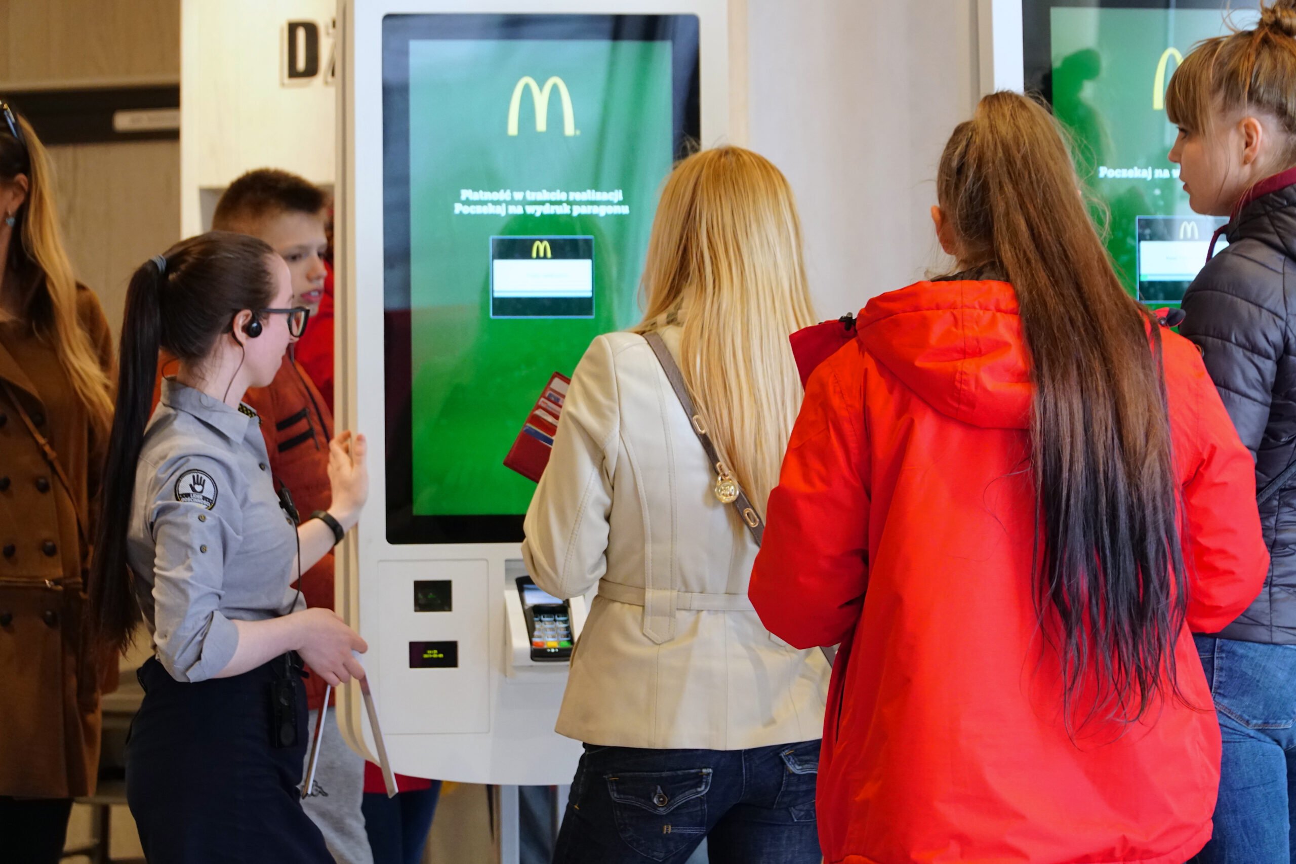 Grupa ludzi korzystająca z samoobsługowego kiosku w restauracji McDonald's.